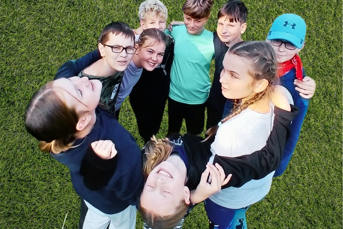 Studenti GTNV stojí v kruhu na trávě a s úsměvem se dívají do objektivu